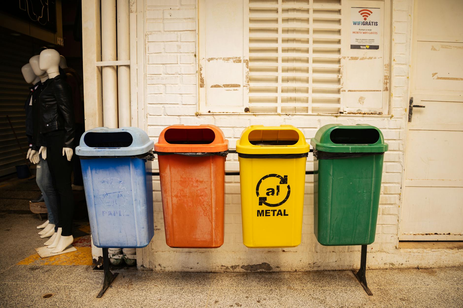 Cztery kolorowe pojemniki do segregacji odpadów przy ceglanej ścianie