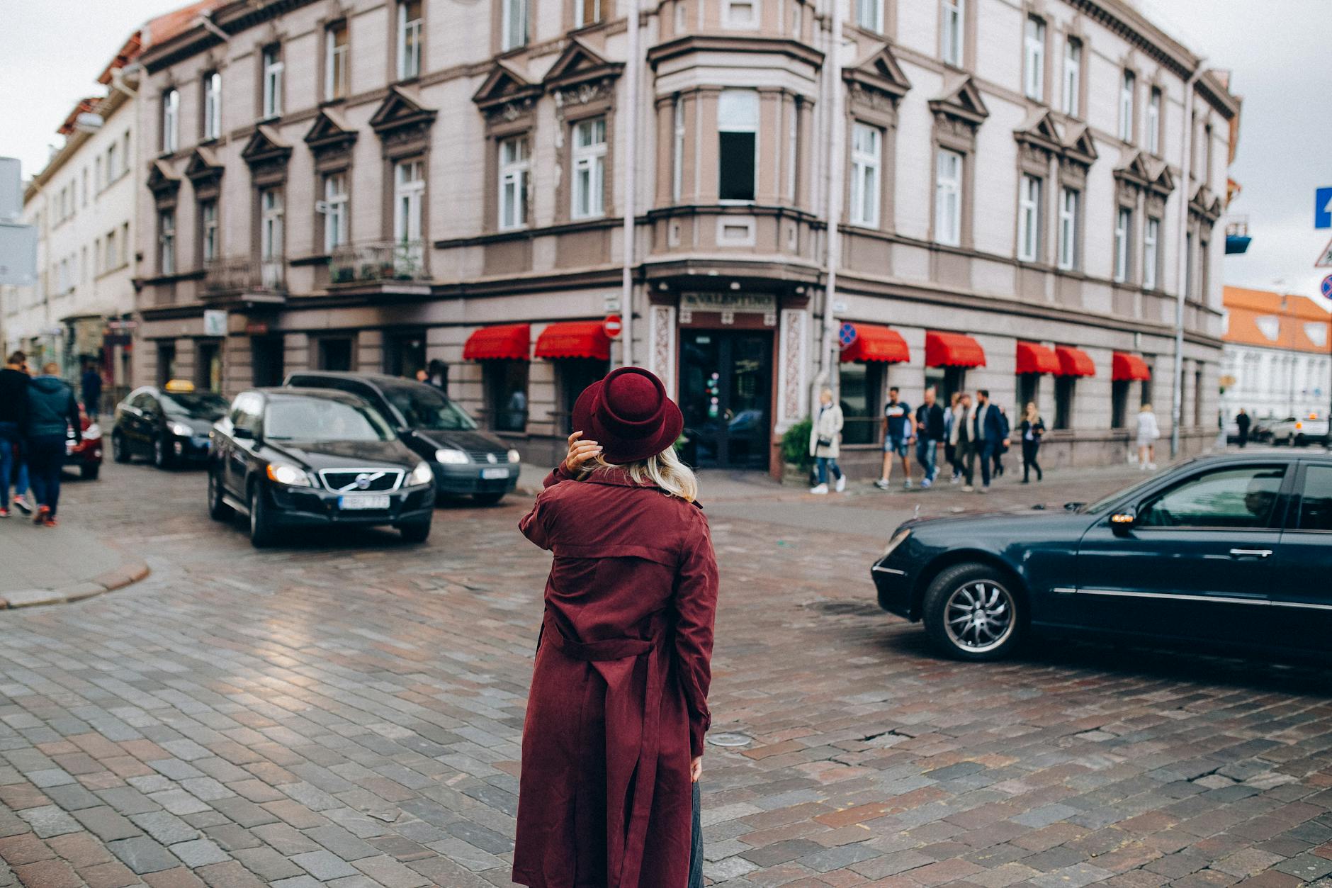 Elegancka kobieta w czerwonym płaszczu i kapeluszu na ruchliwym skrzyżowaniu