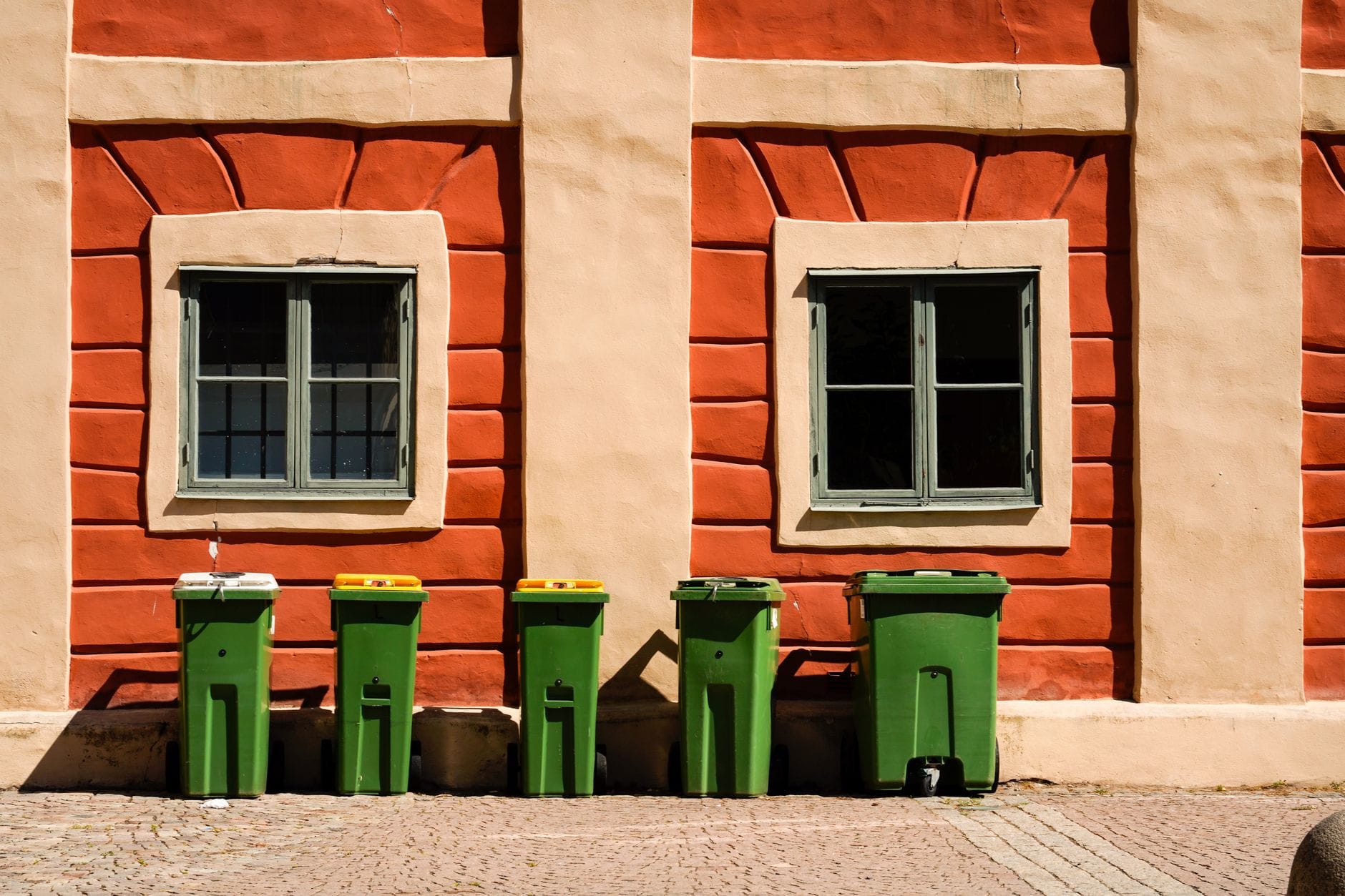Kolorowe pojemniki do recyklingu przy jasnej ścianie w słoneczny dzień