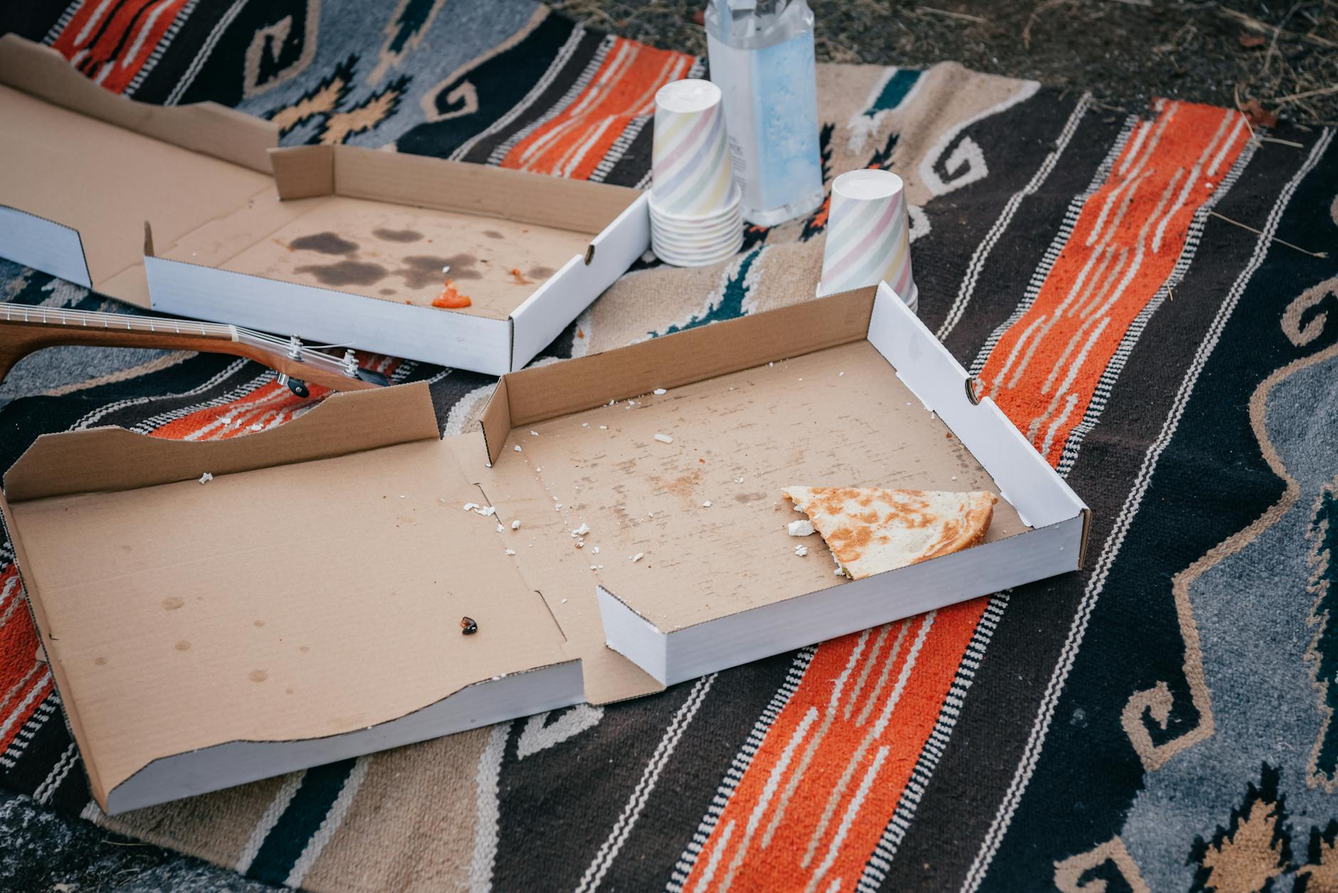 Piknik na kocu z pustymi kartonami po pizzy i papierowymi kubkami