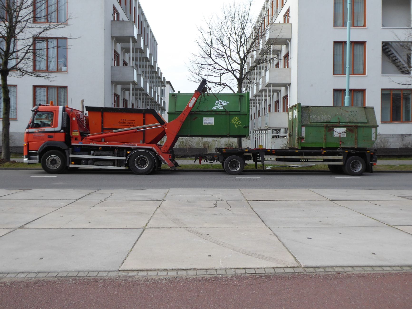 Pomarańczowa śmieciarka z zielonymi kontenerami na ulicy w Amsterdamie