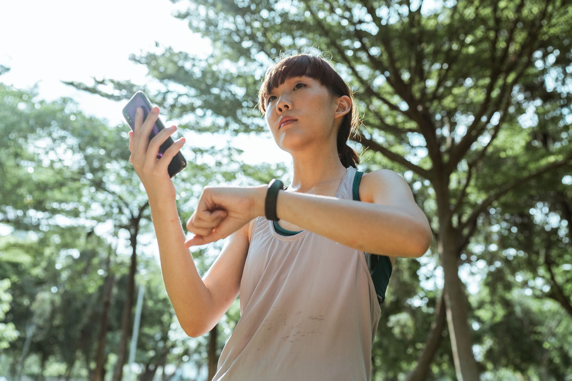 Kobieta w stroju sportowym łączy smartfon ze smartwatchem w parku