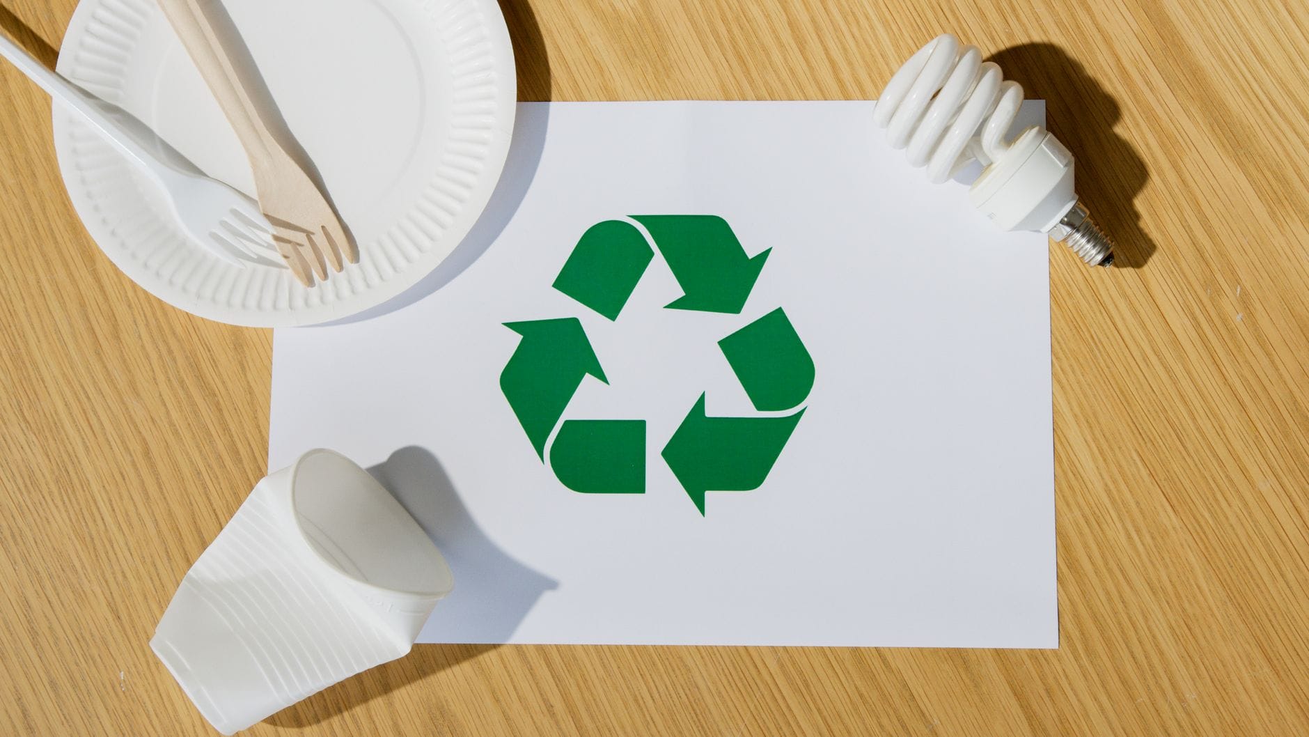 Żarówka i ekologiczne akcesoria obok symbolu recyklingu na kartce papieru