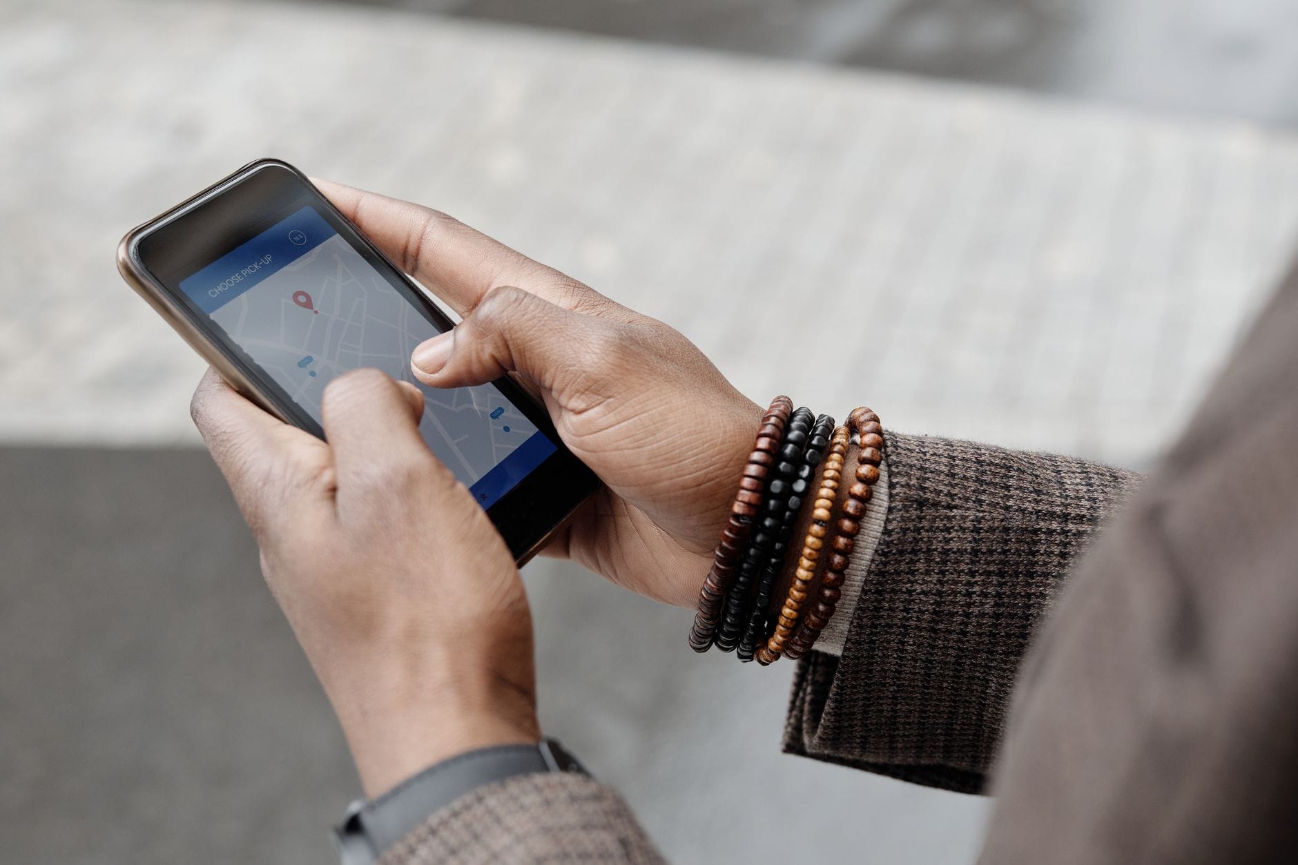 Dłonie z bransoletkami trzymające smartfon z mapą GPS w terenie
